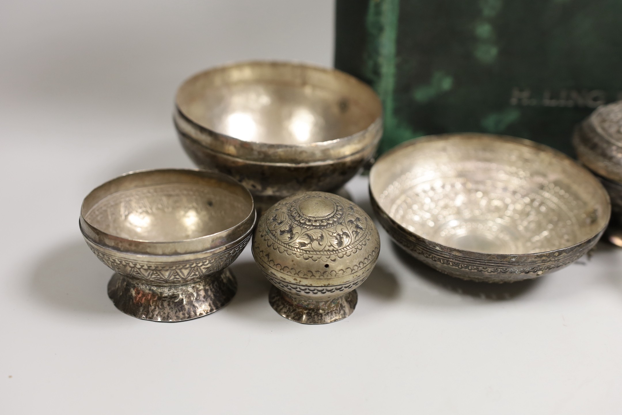 A collection of Malay Straits white metal circular betel nut boxes ('Chimbul'), comprising seven boxes and covers of various sizes (some damaged or missing chain fastenings) and two boxes lacking covers, gross weight 881